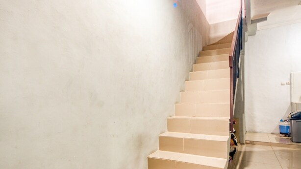 Una escalera con escalones color beige que sube a una plataforma, una barandilla de madera y una pared blanca.