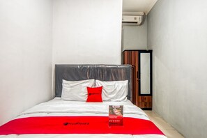 A neatly made bed with a red blanket and a RedDoorz pillow, a wooden wardrobe, and a mirror on the wall. - RedDoorz near Graha Cijantung Mall (Jakarta)