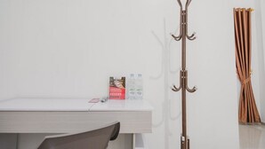 A coat rack with hooks, a white desk with a chair, and a curtain on the wall. - RedDoorz Syariah near Arafah Hospital Jambi (Jambi)