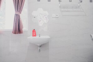 A bathroom with a white sink, a red bottle, and a towel rack. - RedDoorz Syariah near Arafah Hospital Jambi (Jambi)