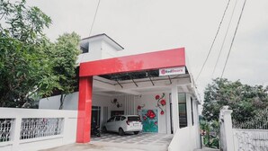A RedDoorz building with a white and red facade, a car parked in front, and a mural of red flowers on the wall. - RedDoorz Syariah near Arafah Hospital Jambi (Jambi)