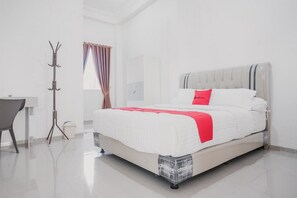 A modern hotel room with a large bed, a desk, and a coat rack. - RedDoorz Syariah near Arafah Hospital Jambi (Jambi)