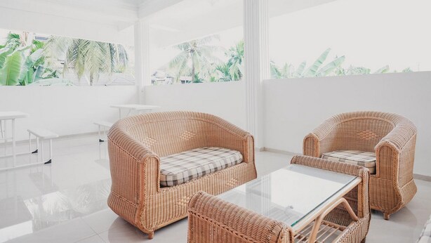 A bright, spacious room with wicker furniture, a glass table, and large windows with a view of tropical plants. - RedDoorz Syariah near Arafah Hospital Jambi (Jambi)