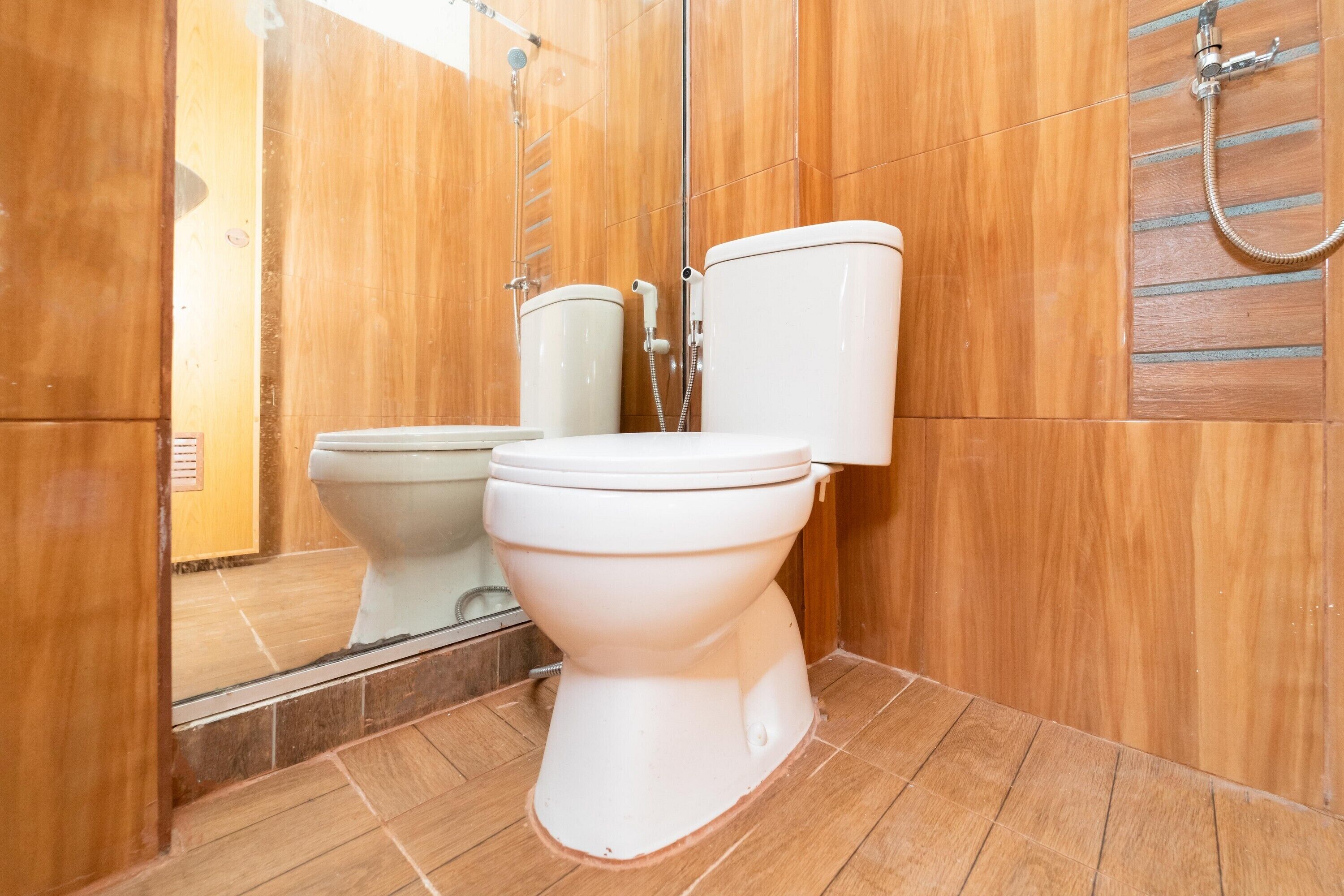A bathroom with wooden walls, a white toilet, and a shower area.
