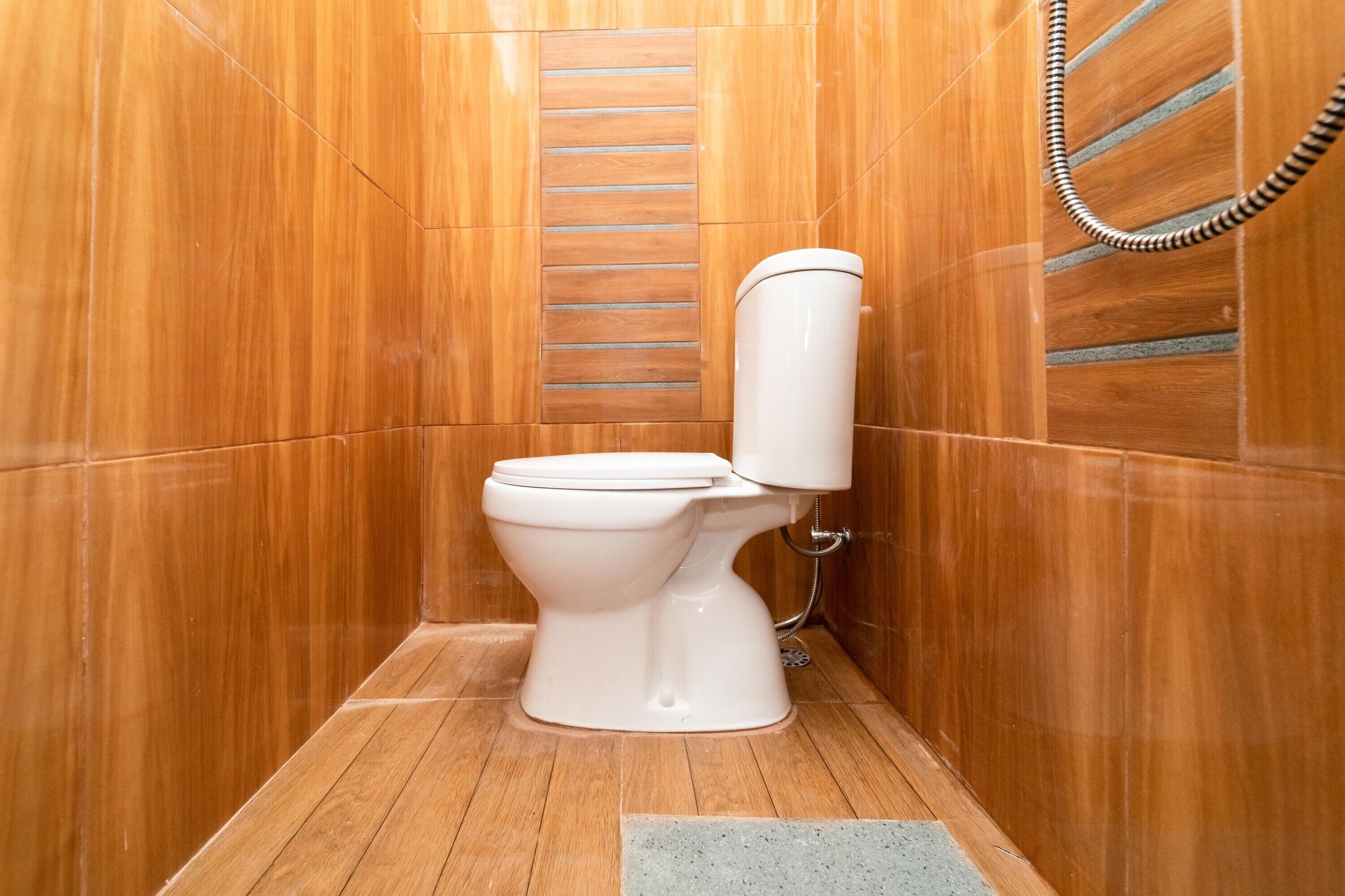 A bathroom with a white toilet, wooden walls, and a shower area.