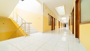 Un largo pasillo bien iluminado con una escalera a la izquierda que conduce a un piso superior. Las paredes están pintadas de amarillo y hay puertas a lo largo del pasillo.