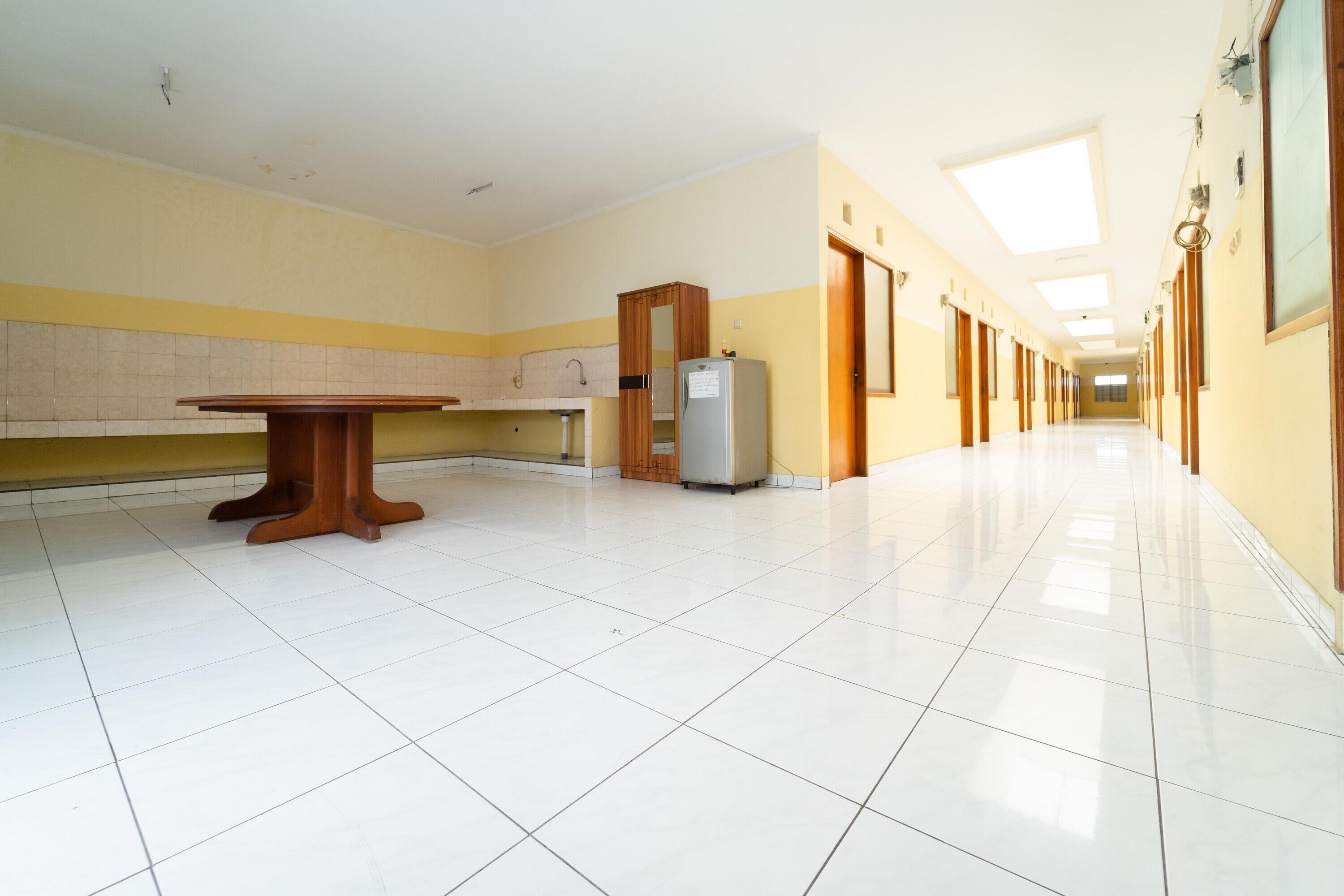 A long, narrow hallway with a tiled floor, a wooden table, a refrigerator, and a wooden cabinet.