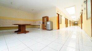 Un pasillo largo y estrecho con suelo de baldosas, una mesa de madera, un refrigerador y un mueble de madera.