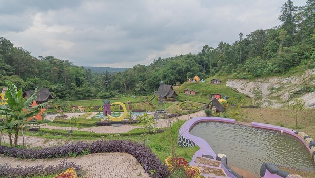 Un jardín ajardinado con un estanque, senderos y pequeñas construcciones.