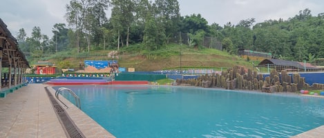 A swimming pool with a tiled deck and a view of a forested hill in the background.