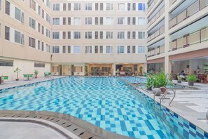 Una amplia piscina interior con baldosas de diseño cuadriculado, rodeada por un edificio de varios pisos con balcones y una zona de estar con plantas.