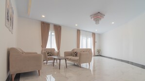 A spacious, well-lit room with beige sofas, a small round table, and a chandelier.