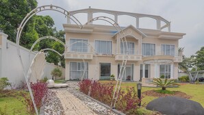 A multi-story house with a symmetrical facade, large windows, and a landscaped garden with a pathway.