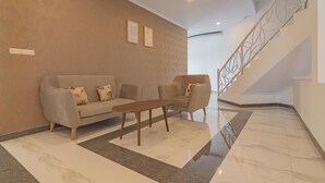 A modern lobby with a sofa and armchairs, a marble floor, and a staircase with a decorative railing.