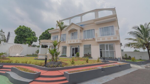 A modern two-story building with a large entrance, a covered patio, and a landscaped garden with pathways and small trees.