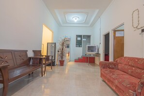 A living room with a wooden bench, a red sofa, a potted plant, and a television on a stand. - RedDoorz @ Rajawali KM 5 (Palangkaraya)