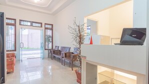 Un hall d’hôtel comprenant un comptoir d’accueil, un ordinateur portable, une plante et un espace détente avec des fauteuils.