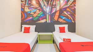 Une chambre d’hôtel avec deux lits, une table de chevet verte et une œuvre d’art abstraite et colorée accrochée au mur.