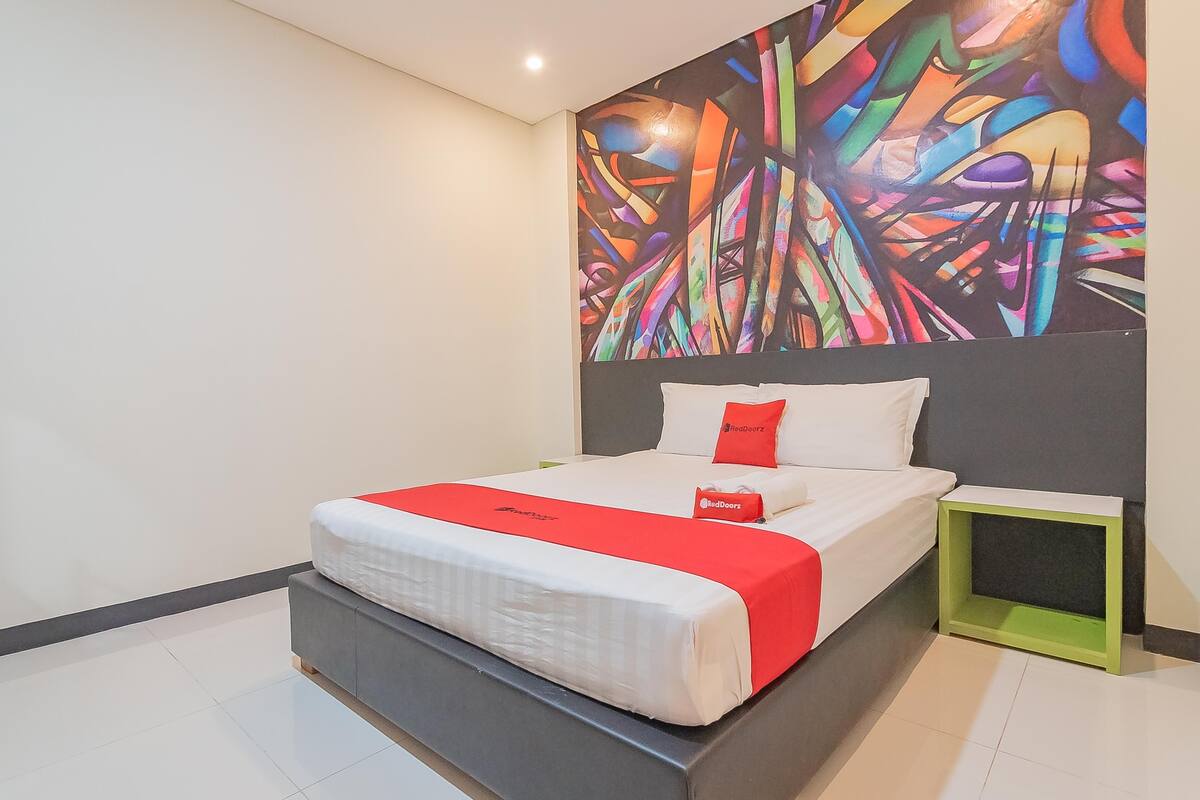 A modern hotel room with a large bed, a colorful abstract mural on the wall, and a small green nightstand.