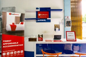 A reception desk with RedDoorz branding, a service guarantee sign, and a framed partnership certificate. - RedDoorz near Benteng Van Den Bosch (Ngawi)