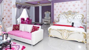 A luxurious bedroom with a white bed, a pink sofa, and a chandelier. - RedDoorz Premium @ Sea Residence Manado (Manado)