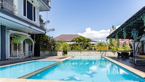 A swimming pool with a tiled deck, surrounded by a stone wall and a building with a balcony. - RedDoorz Premium @ Sea Residence Manado (Manado)