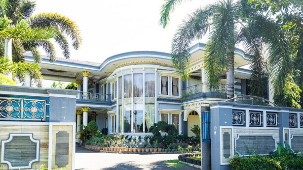 A large, curved building with multiple balconies, a covered entrance, and a well-maintained garden with palm trees and potted plants. - RedDoorz Premium @ Sea Residence Manado (Manado)