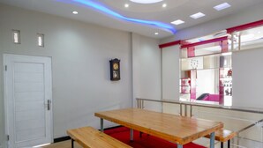 A room with a wooden table and bench, a white door, a clock on the wall, and a red carpet. - RedDoorz Syariah near Komplek Candi Arjuna Dieng (Dieng Kulon)