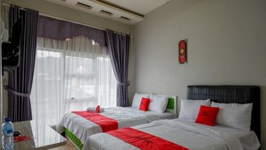 A hotel room with two beds, a small table, and a window with curtains. - RedDoorz Syariah near Komplek Candi Arjuna Dieng (Dieng Kulon)