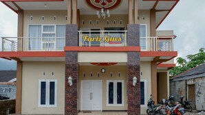 A two-story building with a sign reading "Fariq Gues House". There are two white doors, a balcony with a railing, and a staircase leading to the upper floor. - RedDoorz Syariah near Komplek Candi Arjuna Dieng (Dieng Kulon)