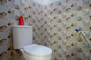 A bathroom with a toilet, a red bottle on the tank, and a shower with a hose.