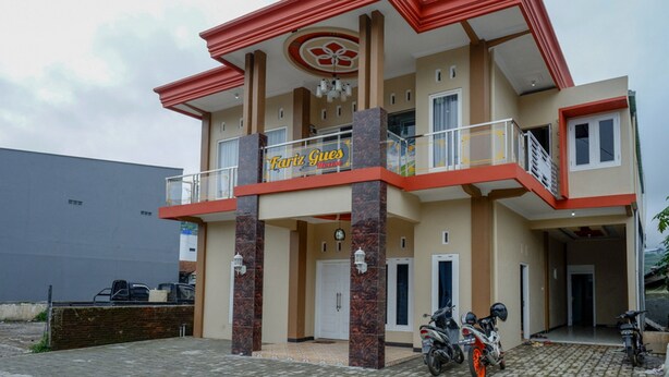 A two-story building with a red and beige facade, a balcony, and a sign that reads "Fariz Gues House". - RedDoorz Syariah near Komplek Candi Arjuna Dieng (Dieng Kulon)