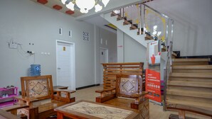 A spacious room with a wooden staircase, a large wooden table, and a red carpet. - RedDoorz Syariah near Komplek Candi Arjuna Dieng (Dieng Kulon)