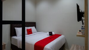 Ein Hotelzimmer mit einem Bett, einer roten und weißen Tagesdecke, einem Holz-Kopfteil, einem an der Wand befestigten Fernseher und einem kleinen Holzboden mit Toilettenartikeln.