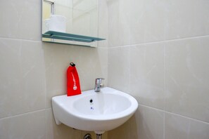 A bathroom with a white sink, a glass shelf above it, and a red bag hanging on the wall.