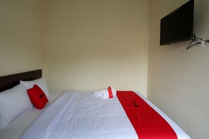A neatly made bed with white and red bedding, a red pillow, and a towel on the side.