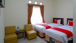 A hotel room with two beds, a small table with a chair, and a window with curtains.