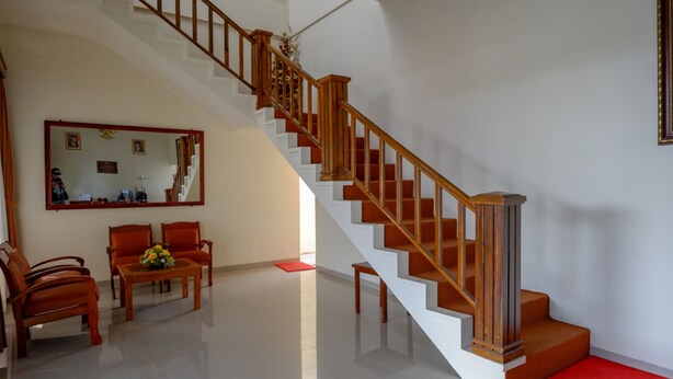 A spacious living area with a wooden staircase, a dining table with chairs, and a red carpet leading to the stairs.