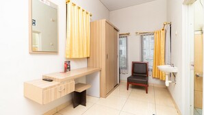 A small, clean room with a wooden desk, a chair, a mirror, a wardrobe, and a bathroom with a sink and curtains. - RedDoorz Plus @ Jalan Pumorow Manado (Manado)