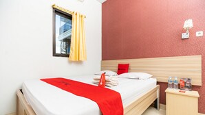 A hotel room with a bed, a nightstand, a window with yellow curtains, and a red wall. - RedDoorz Plus @ Jalan Pumorow Manado (Manado)