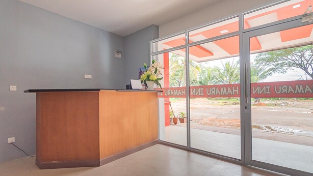 A reception area with a wooden desk, a potted plant, and a large glass door leading outside. - RedDoorz @ Pasar Melayu Sagulung Batam (Batam)