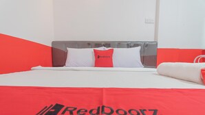 A bed with a white and red bedspread, a pillow with the RedDoorz logo, and a white towel. - RedDoorz @ Pasar Melayu Sagulung Batam (Batam)