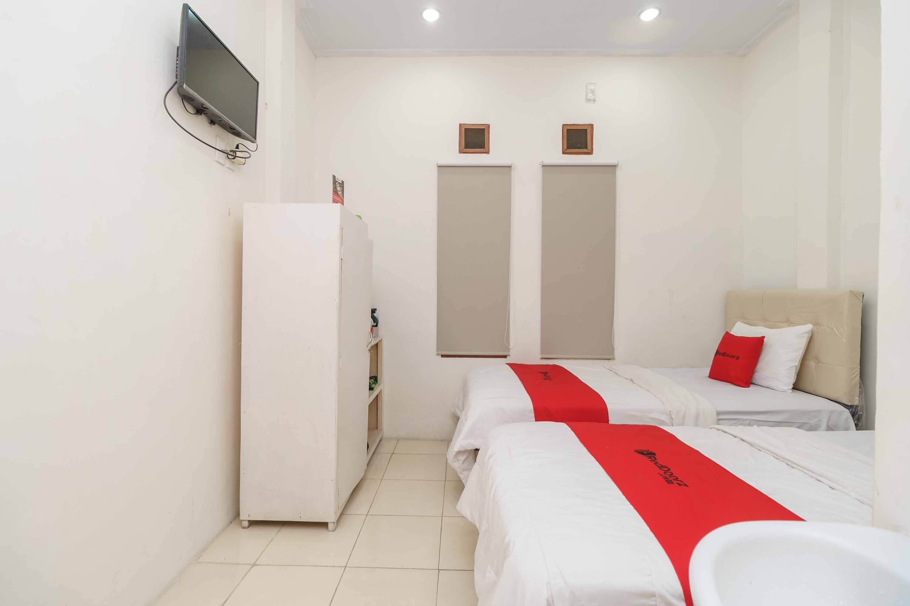 Habitación de hotel con dos camas, un televisor montado en la pared y un armario.