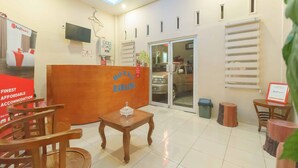 A hotel reception area with a wooden reception desk, a TV mounted on the wall, and a glass door leading to the parking area.
