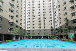 A swimming pool surrounded by high-rise residential buildings with balconies. - RedDoorz Apartment @ Gateway Cicadas (Bandung)