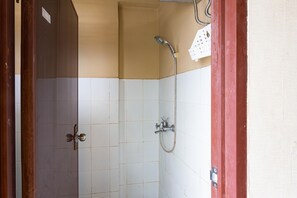 A bathroom with white tiled walls, a shower with a handheld showerhead, and a red door frame. - RedDoorz Apartment @ Gateway Cicadas (Bandung)