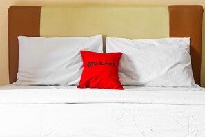 A bed with white bedding and a red pillow with "RedDoorz" text. - RedDoorz Apartment @ Gateway Cicadas (Bandung)