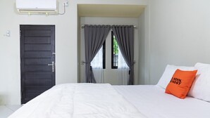 Habitación de hotel con cama, ventana con cortinas, puerta y unidad de aire acondicionado.