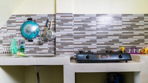 Una cocina con estufa a gas, cilindro de gas azul, un lavabo y un escurreplatos.