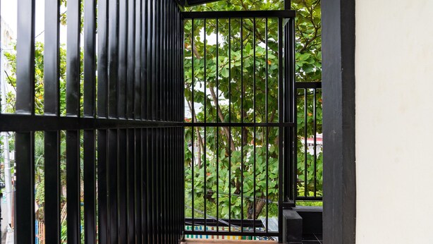 Una escalera de madera que conduce a un balcón con barandilla de metal negro, rodeado de abundante follaje verde.